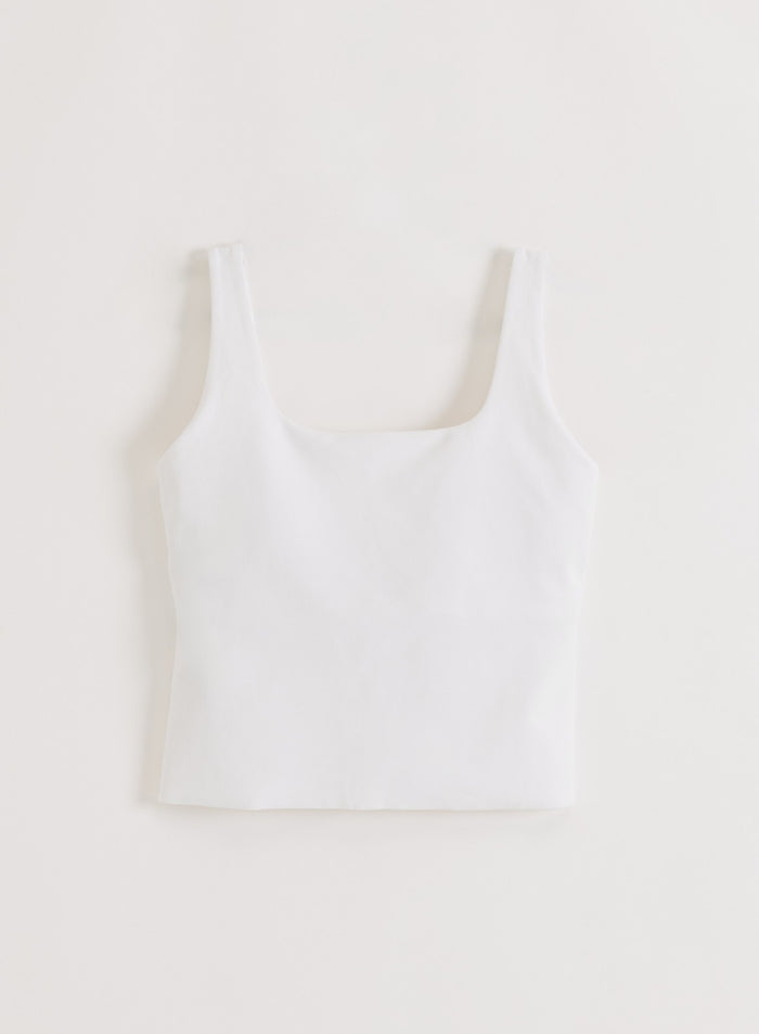 Minimalistinen valkoinen aim'n Sense Singlet pyöreällä pääntiellä ja paksuilla olkaimilla flat lay -kuvassa.
