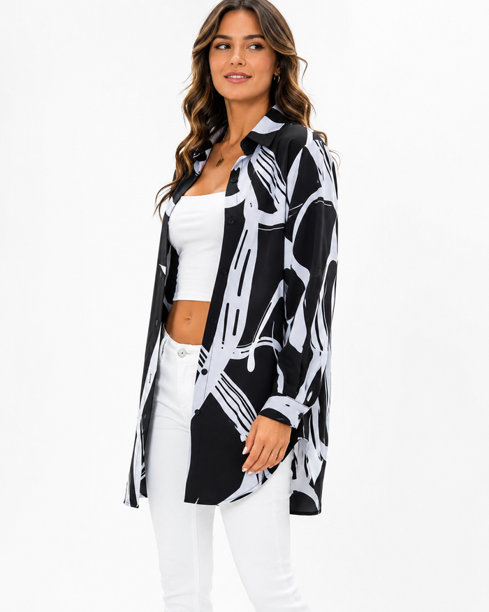A woman modeling a black and white abstract print button-up shirt over a white crop top and white pants, photographed against a plain white studio background.