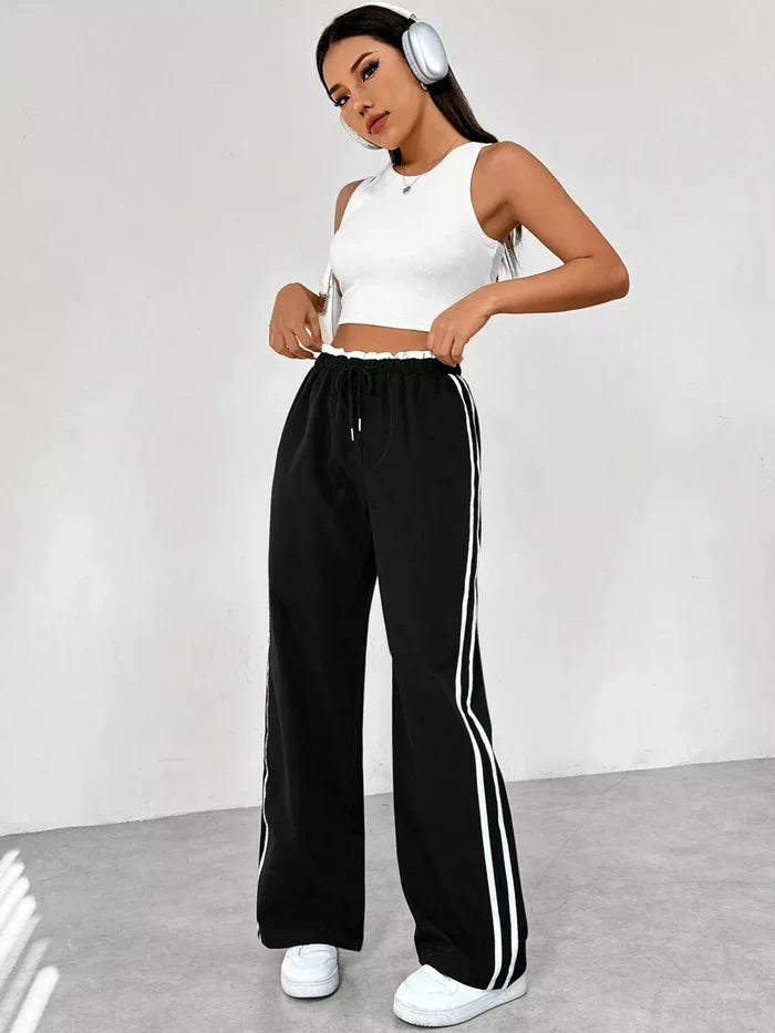Woman wearing a white crop top and black pants with white stripes, standing against a plain background.